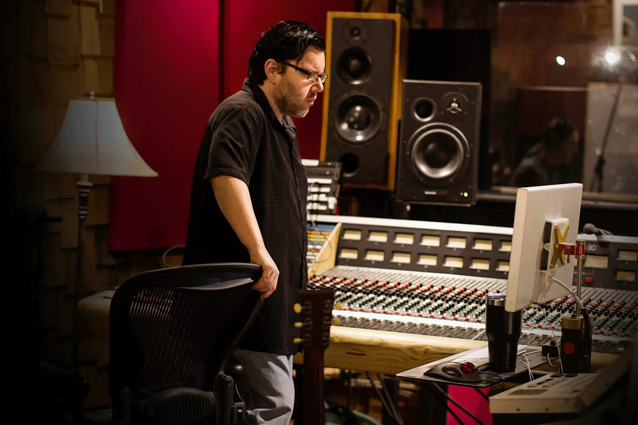 Jack Miele standing at a large analog mixing console, focused on a computer monitor in the control room